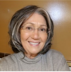 A woman with gray hair and glasses smiling.